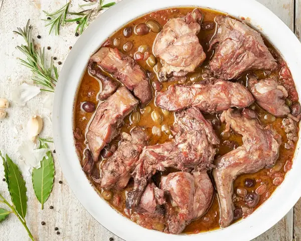 Coniglio in padella, un piatto succulento con olive e aromi, pronto per essere gustato.