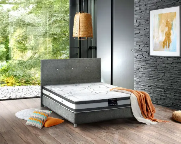 Un lit moderne avec un matelas de dimension queen size, des coussins colorés et une couverture orange sur un parquet en bois.