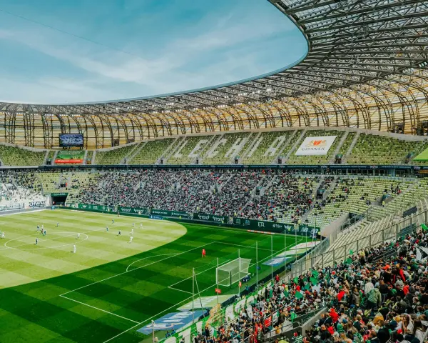 Widok na murawę i trybuny Polsat Plus Arena Gdańsk podczas meczu. Tłumy kibiców na zielonych krzesełkach.