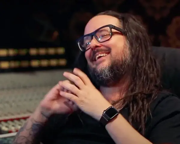 Jonathan Davis, le chanteur de Korn, rit en studio d'enregistrement, lunettes sur le nez et longue chevelure brune.