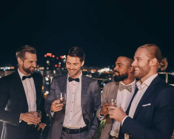 Eleganccy panowie w garniturach i muszkach, pijący drinki na tarasie. Idealny przykład, jak się ubrać na poprawiny.
