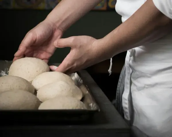 Mani esperte sistemano impasti per pizza, un mestiere che fa riflettere su quanto guadagna un pizzaiolo al mese.