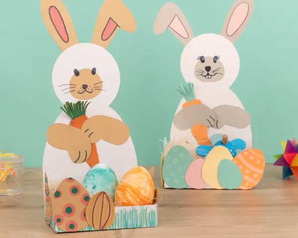 Zwei süße Osterhasen halten Karotten. Kinder haben diese tollen Osterdeko zum Thema Osternest basteln Kinder selbst gemacht.