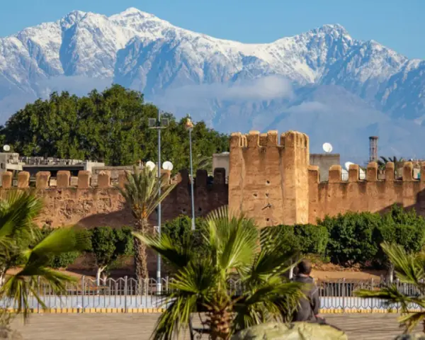 Marrakesz, gdzie leży, widać na tle ośnieżonych gór Atlas. Stare mury miasta i palmy tworzą malowniczy krajobraz.