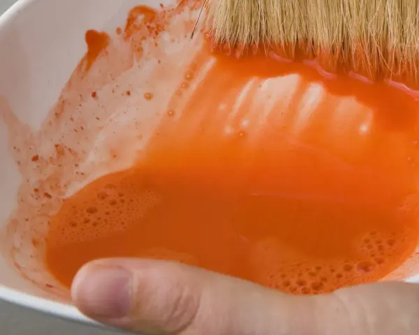 Maintenant, où jeter l'eau de rinçage des pinceaux ? Une main tient un bol blanc rempli d'eau orange trouble.