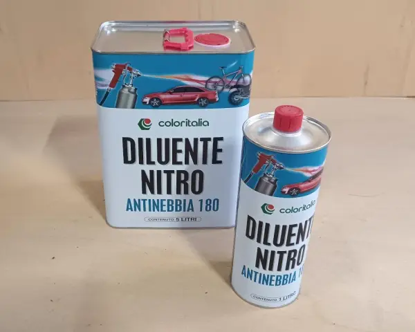 Due barattoli di diluente nitro Coloritalia, uno da 5 litri e uno da 1 litro, con grafica di auto e bici. La differenza tra diluente sintetico e nitro è nella composizione.