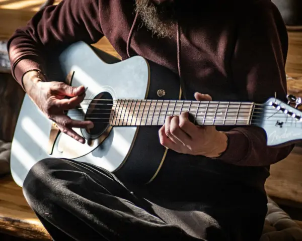Mann spielt Akustikgitarre, Hände auf Saiten und Plektrum.
