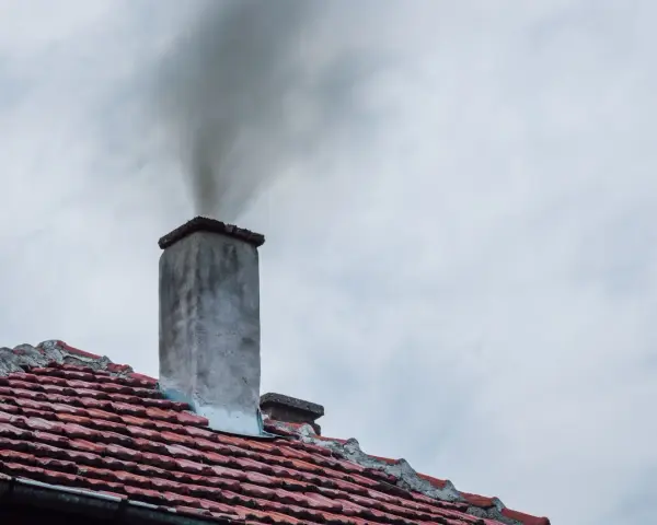 Dym wydobywający się z komina na tle pochmurnego nieba.