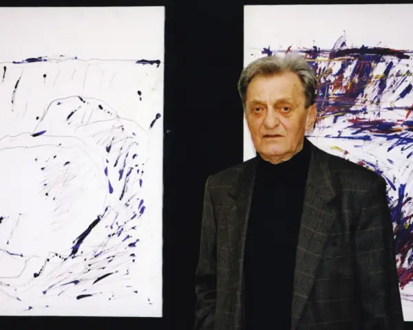 Jacek Sempoliński, artysta, stoi obok swoich abstrakcyjnych obrazów.