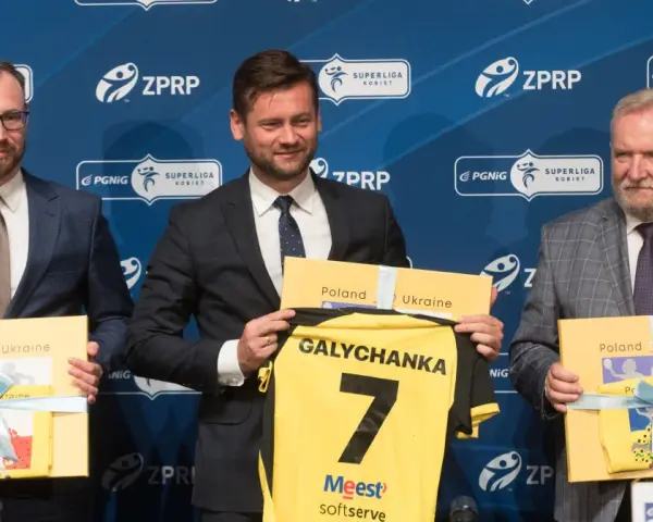 Trzech mężczyzn w garniturach prezentuje koszulkę z napisem "Galychanka" i numerem 7. Obok nich żółte pudełka z napisami "Poland Ukraine".