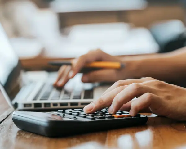 Hände bedienen Laptop und Taschenrechner. So lässt sich die Kaution in Raten zahlen und die Finanzen im Blick behalten.
