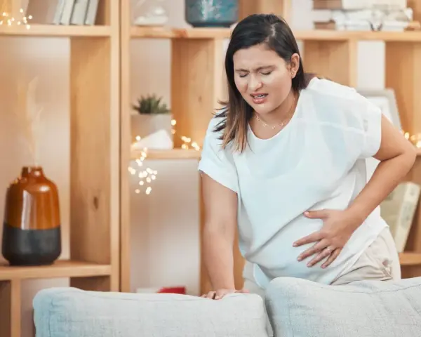 Frau mit schmerzverzerrtem Gesicht hält ihren Bauch, als ob sie Wehen erkennen würde.