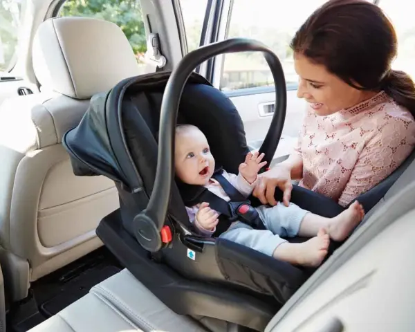 Uśmiechnięta mama patrzy na swojego **noworodka w foteliku samochodowym**, gotowego na podróż.