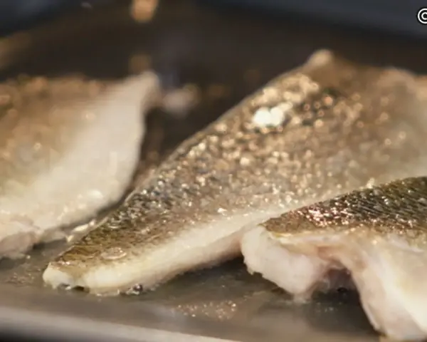 Filetes de lubina a la donostiarra dorándose en una sartén.