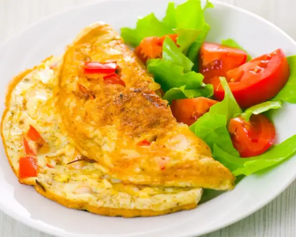 Złocisty omlet francuski z kawałkami papryki, podany z sałatką z pomidorów i sałaty. Pyszne śniadanie.