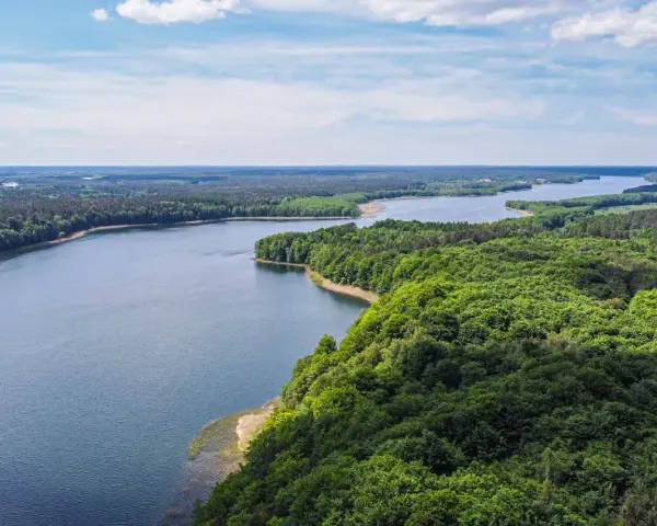 Malownicze jezioro otoczone lasem, idealne miejsce na nietypowe atrakcje Mazury. Widok z lotu ptaka na spokojną taflę wody i bujną zieleń.