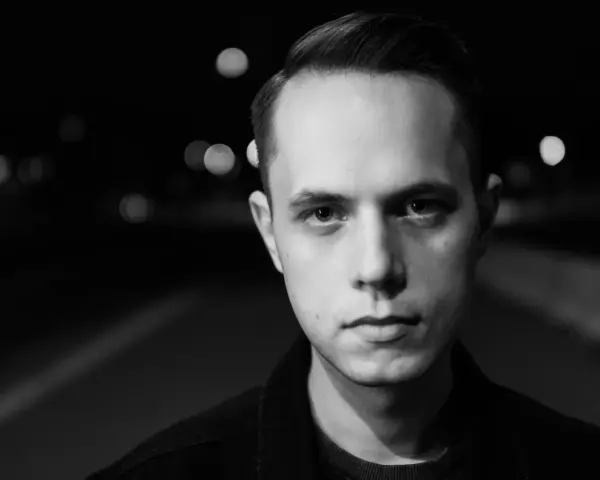 Młody mężczyzna, Gibbs producent, patrzy wprost w obiektyw na tle nocnych świateł.