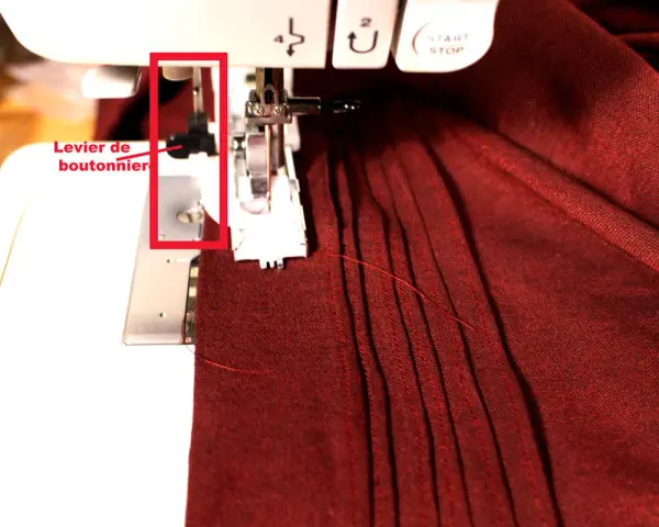 Levier de boutonnière sur machine à coudre, prêt pour réaliser une boutonnière parfaite sur un tissu bordeaux plissé.