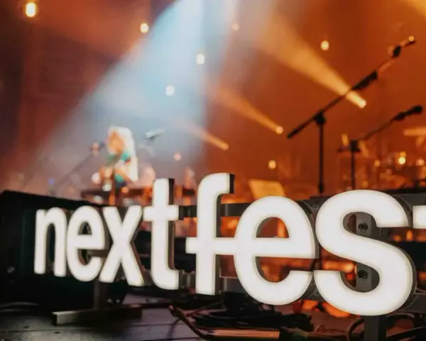Światła sceny oświetlają napis "next fest" i artystkę grającą na gitarze.