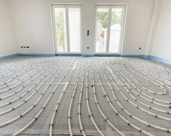 Instalacja ogrzewania podłogowego w bloku. Białe rurki ułożone na siatce tworzą wzór, przygotowane do wylania posadzki.
