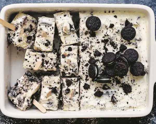 Oreo glass recept: krämig glass med krossade Oreos och hela kakor, skuren i bitar med träpinnar. Perfekt sommardessert!