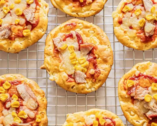 Mini pizze z serka wiejskiego, z kukurydzą i kawałkami mięsa, na metalowej kratce.