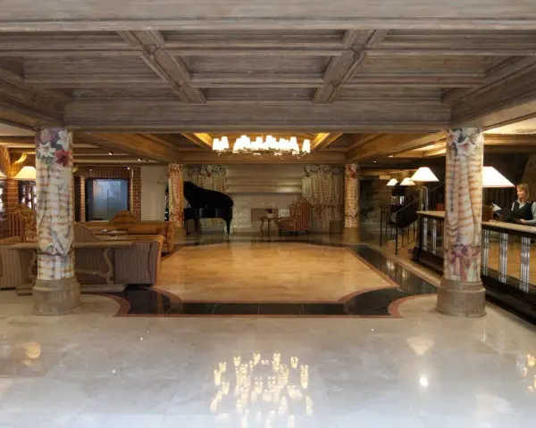 Eleganckie lobby hotelowe z fortepianem, recepcją i dwoma pracownikami.