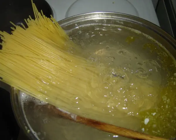 Długi makaron spaghetti gotuje się w bulgoczącej wodzie. Czas, **ile gotować makaron**, zależy od jego grubości.