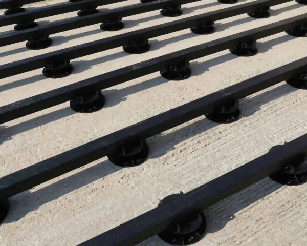 Rows of black synthetic lumber are elevated on black adjustable pedestals, creating a modern deck base on a concrete surface.
