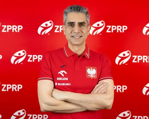 Uśmiechnięty mężczyzna, były trener piłkarzy ręcznych, w czerwonej koszulce z godłem Polski i logo ZPRP.