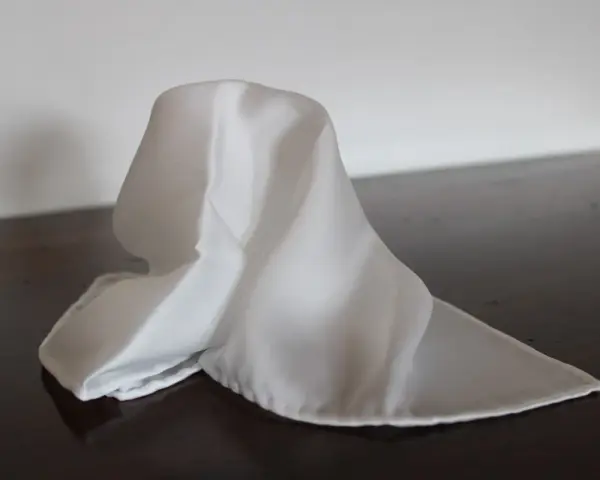 Un fazzoletto bianco di seta, drappeggiato su un tavolo scuro. Il suo significato è legato alla purezza e all'eleganza.
