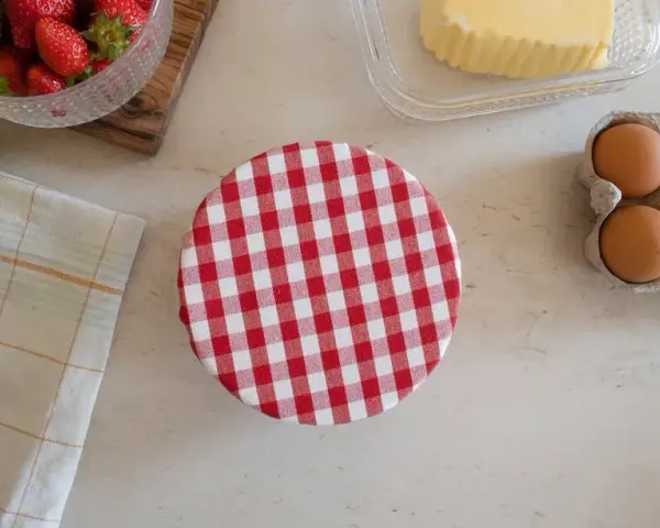 Préparation d'une charlotte alimentaire : fraises, citron, beurre, œufs et un couvercle à carreaux rouges et blancs.
