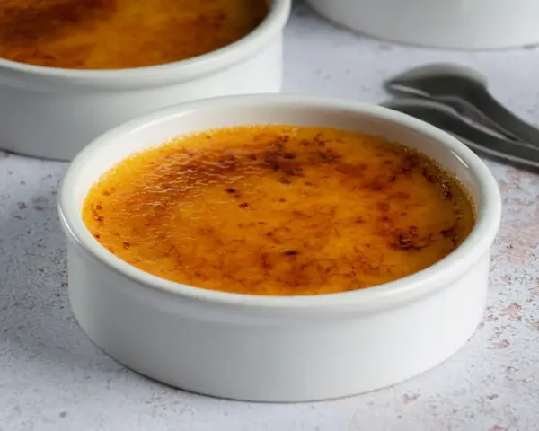 Dwa kremowe desery w białych naczyniach, z chrupiącą, karmelizowaną skórką. Crème brûlée czy crema catalana? Wybór należy do Ciebie!