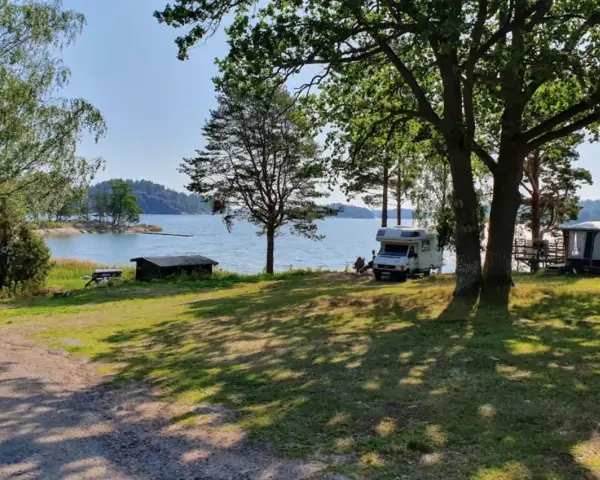 Solig dag vid vattnet på Kalvholmens camping. Husbilar och husvagnar står uppställda på gräsmattan nära sjön.