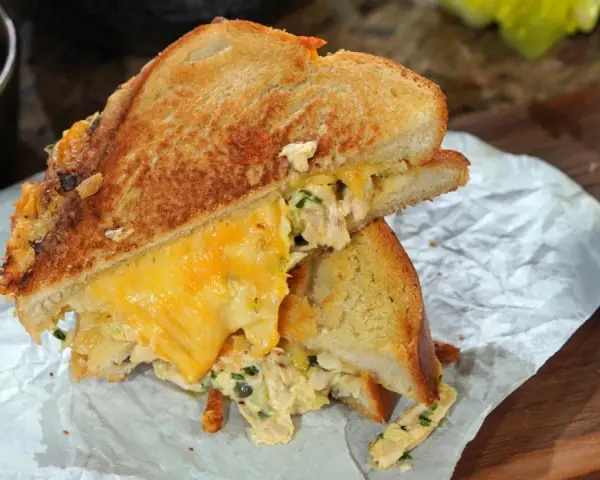 Ein köstlicher Tuna Melt mit geschmolzenem Käse, serviert mit Gurken und Chips.