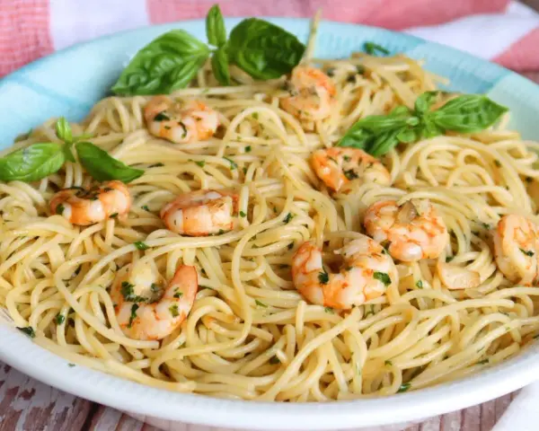 Un plato de espaguetis con gambas, adornado con hojas de albahaca fresca y perejil picado.