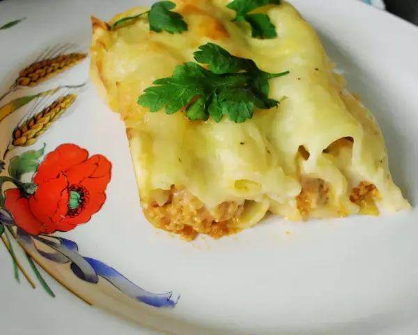 Cannelloni z mięsem i beszamelem przepis. Pyszne danie zapieczone pod beszamelem, udekorowane natką pietruszki, na talerzu z makami.