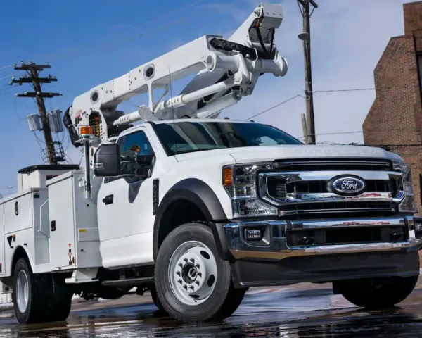Biały Ford F-750 z podnośnikiem koszowym gotowy do pracy przy liniach energetycznych.