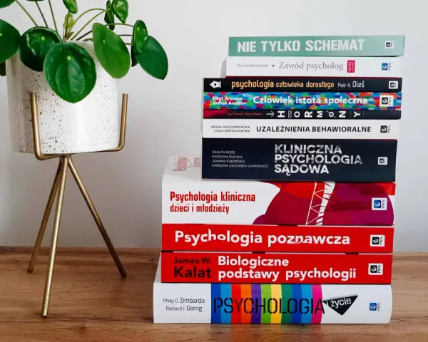 Stos książek do studiów psychologicznych, od psychologii społecznej po kliniczną, obok rośliny w doniczce.
