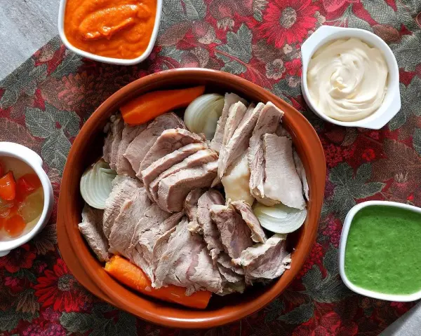 Un invitante bollito di carne, affettato e servito con carote, cipolle e tre salse: una rossa, una bianca e una verde.