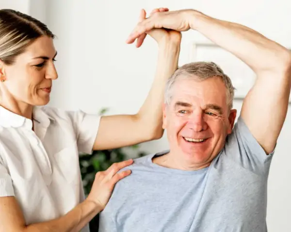 Physiotherapeutin unterstützt Mann bei Übungen zur Wiederherstellung der Beweglichkeit nach Schlaganfall. Verordnung Physiotherapie nach Schlaganfall wird umgesetzt.