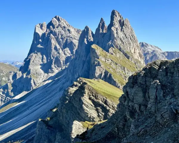 Majestätische Felszinnen ragen in den blauen Himmel. Eine **Seceda Wanderung** führt durch grüne Almwiesen und felsiges Gelände.
