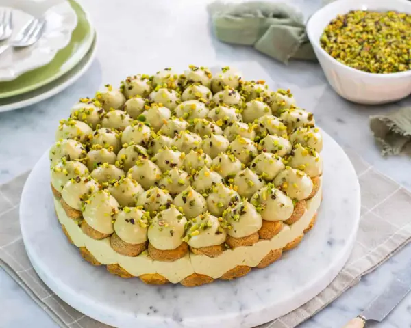 Torta rotonda con tante piccole meringhe verdi e granella di pistacchio, un delizioso tiramisù al pistacchio.
