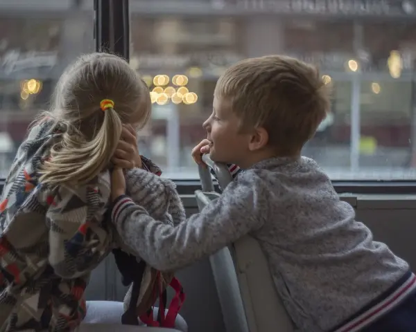 Bambina con disturbo della comunicazione sociale si nasconde, mentre un bambino le parla con un sorriso.