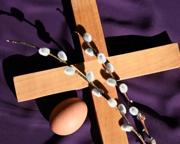 Holzkreuz mit Weidenkätzchen und Ei auf lila Stoff, ein Symbol für christliche Ostern.