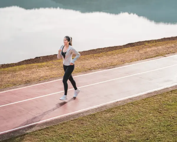 Une femme souriante profite d'une marche rapide sur une piste de course, au bord d'un lac paisible.