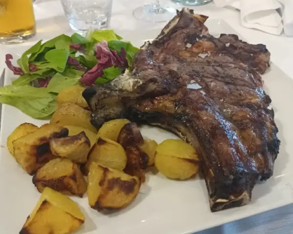 Succulenta costata di manzo alla griglia, servita con patate arrosto croccanti e un'insalata fresca. Un piatto da vero intenditore.