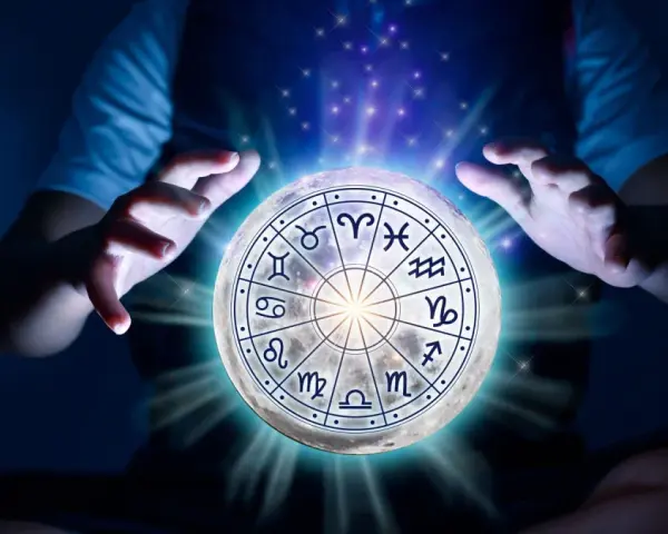 Dłonie unoszą księżyc z tarczą zodiaku, gdzie znaki zodiaku i żywioły splatają się w mistycznym świetle.