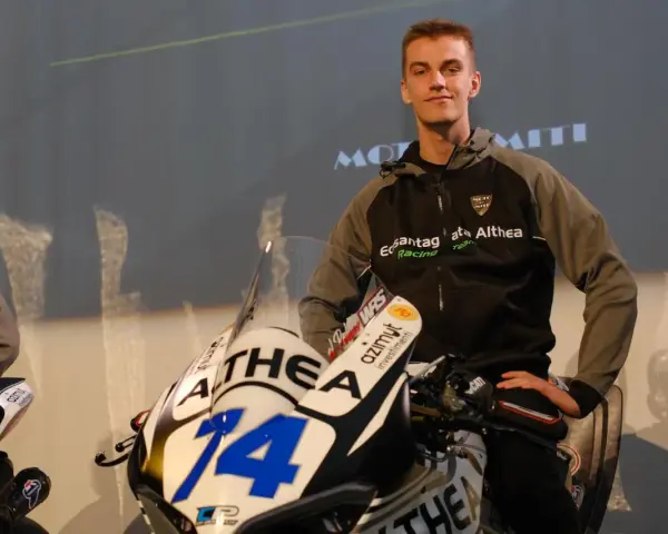 Piotr Biesiekirski, młody kierowca wyścigowy, pozuje obok swojego motocykla z numerem 14.