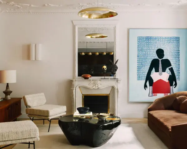 Un dormitorio eclectico con sofá marrón, dos sillones de tweed, mesa de centro de piedra negra, chimenea de mármol y arte abstracto vibrante.